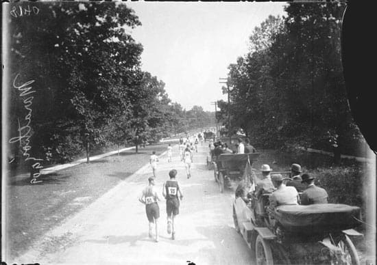 marathoners next to early automobiles